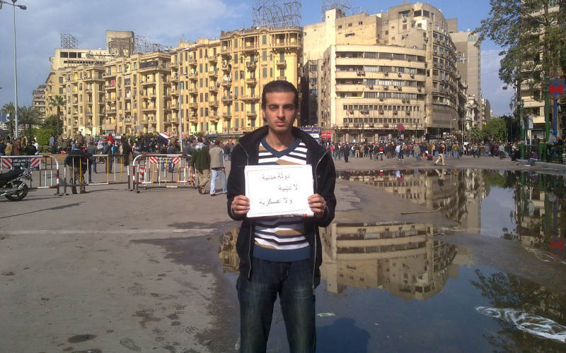 A young man has an embassy in the Egyptian language in his hands. In the background, an architectural cityscape can be seen.