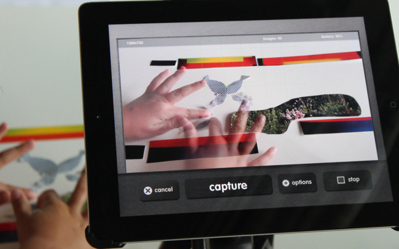 Per iPad werden zwei Kinderhände aufgezeichnet, die an einer Papiercollage arbeiten.