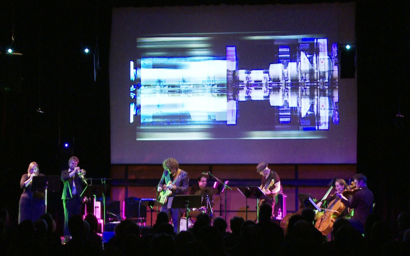 Musical band on a stage. Above them in the background futuristic video animations.