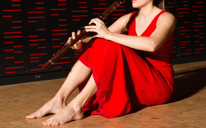 A woman dressed in red sitting on the floor. In her hands she holds a flute. 
