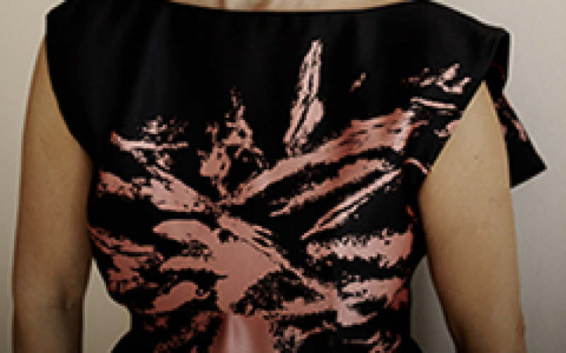 Half portrait of a woman. She wears her hair closed. Her black sleeveless top has a dusky pink-colored abstract print.