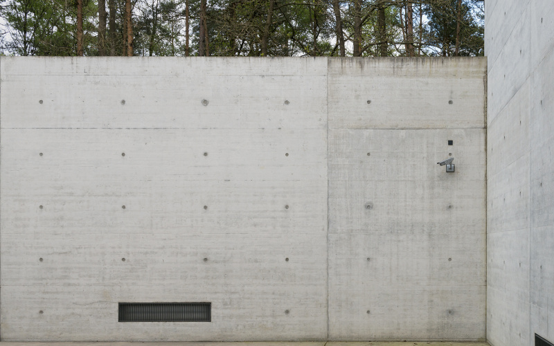 Eine Betonmauer mit einer Lüftung links und einer Überwachungskamera rechts oben
