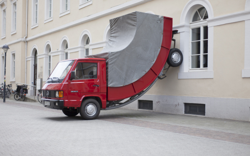 Ein roter Truck, dessen Hinterräder an der Wand stehen.