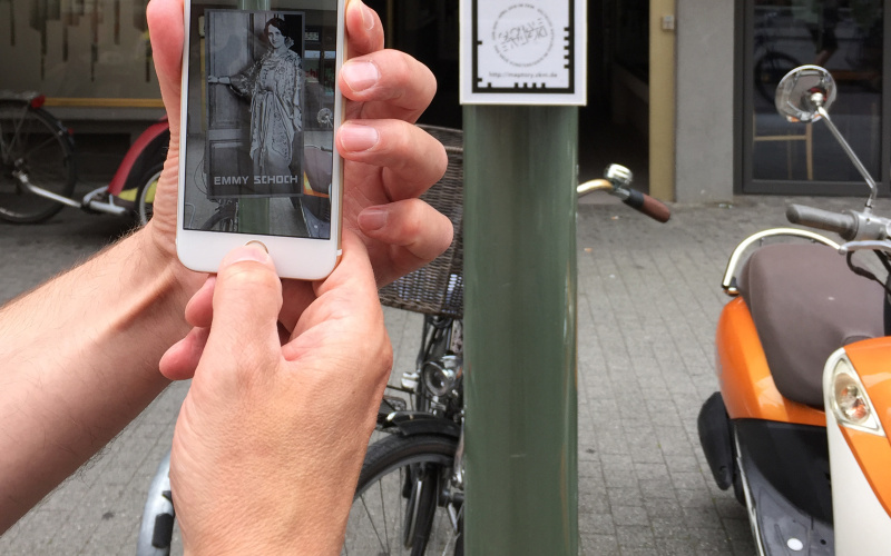 Ein Smarthphone wird hochgehalten, um den Augmented-Reality-Marker auf einer Säule zu erfassen.