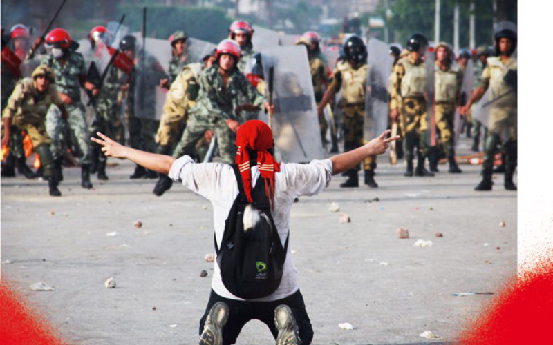  The book cover of "Global Activism" shows a photo: A man is kneeling in the street with both hands up forming the victory sign. He looks at a force of uniformed men.