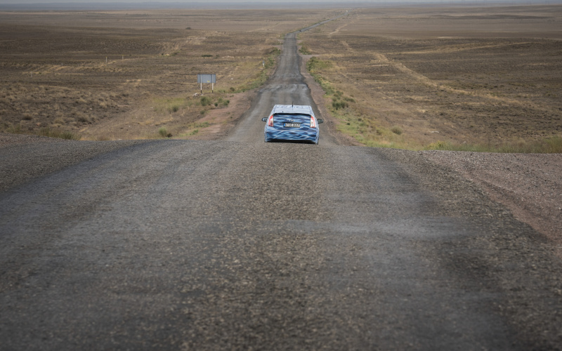 A blue car driving through a desert landscapes