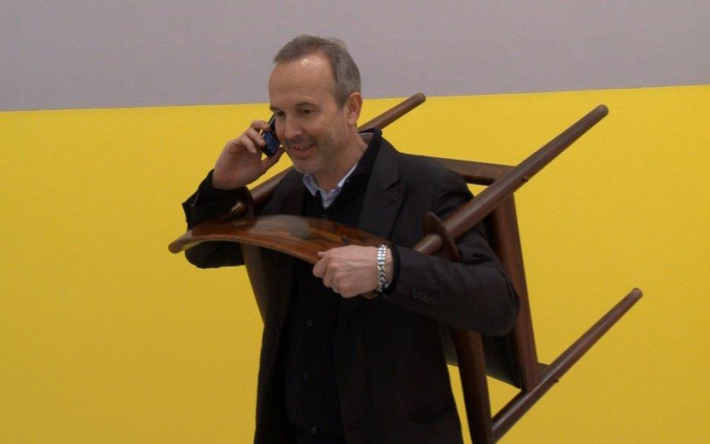 A man at the telephone, wearing a chair around his neck