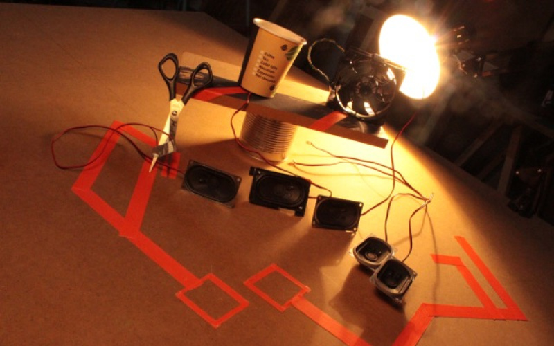Various speaker boxes are illuminated by a desk lamp.