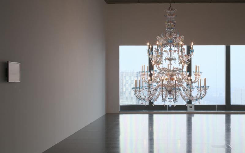 Illuminated chandelier in empty room in front of large windows.