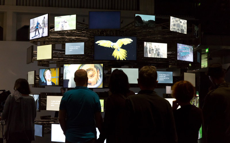  The picture shows visitors in front of a circularly arranged variety of differently screened screens.