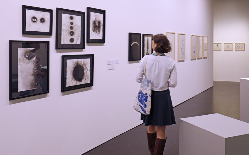 A young woman looks at collages by Gerhard Rühm. 