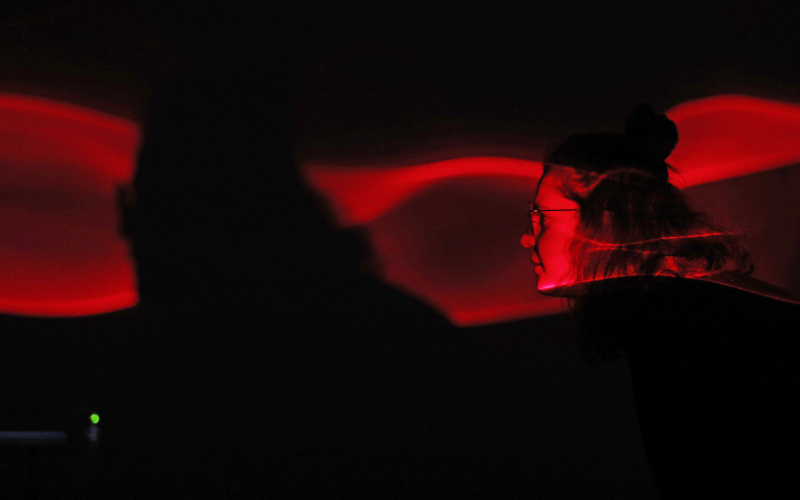  The face of a visitor is red-lit by a broken laser projection.