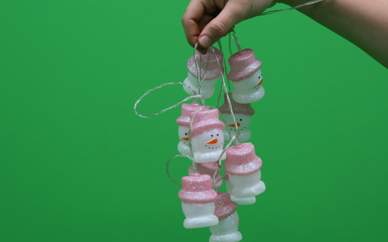 A snowman chain of lights is held in front of a green screen.