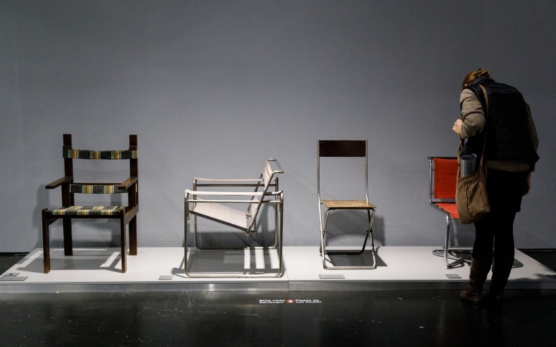 Ausstellungsansicht "Die ganze Welt ein Bauhaus", Frau betrachtet ausgestellte Stuhlmodelle