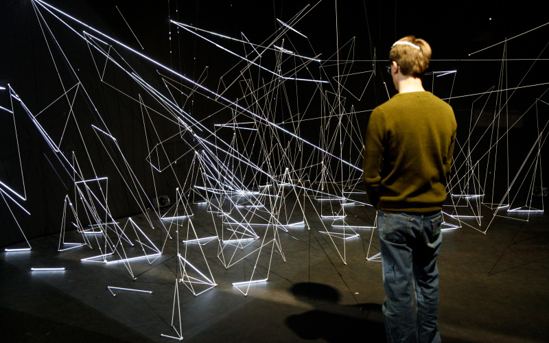An installation of white, illuminated nylon threads in geometric shapes.