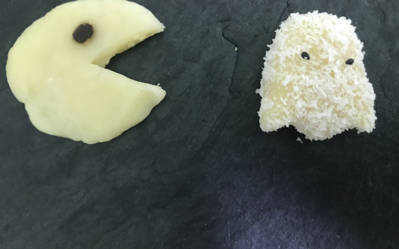 A pacman made of marzipan chases a ghost that is also made of marzipan and sprinkled with coconut flocks.