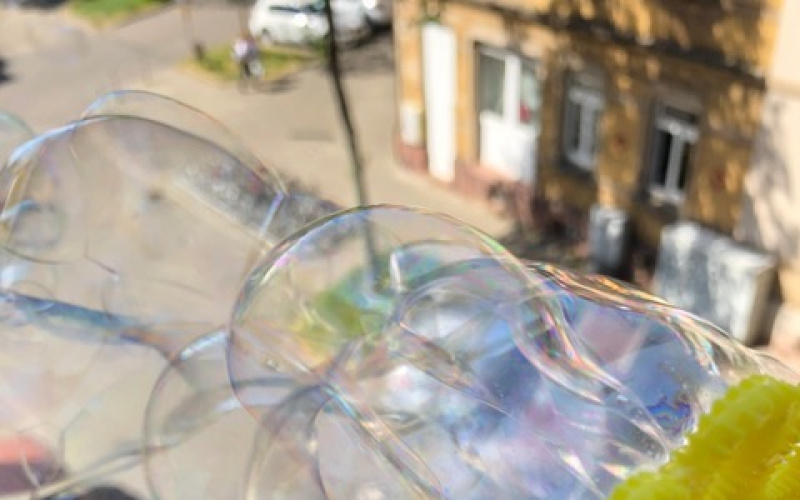 The wind blows many shimmering soap bubbles through a yellow bubble wheel.