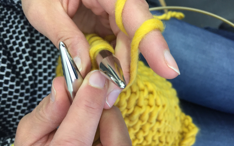 From above two hands are photographed knitting a yellow scarf.