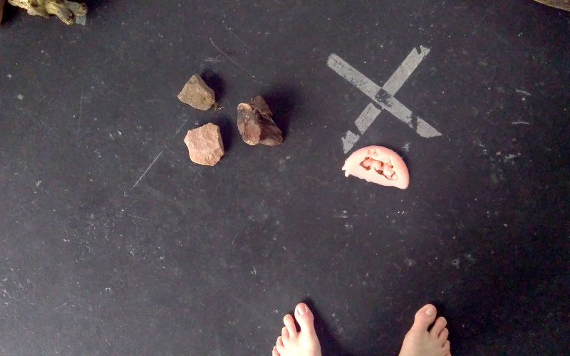 Two pieces of wood, three stones and a pair of feet can be seen on a black background. 