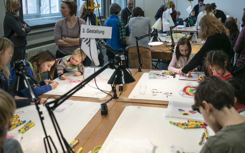 Viele Kinder malen am Tisch bei einem Workshop.