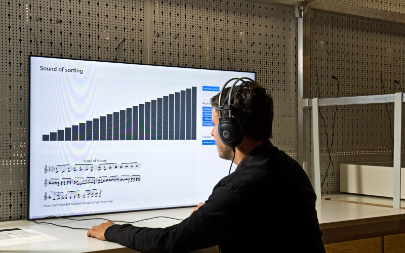 The picture shows a sitting man with headphones in front of a large screen with a sound simulation program