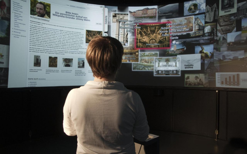 An averted person stands in front of a curved wall with representations of various digital images