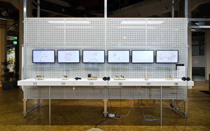 The photo shows six screens on a white grid structure with small objects below and two headphones