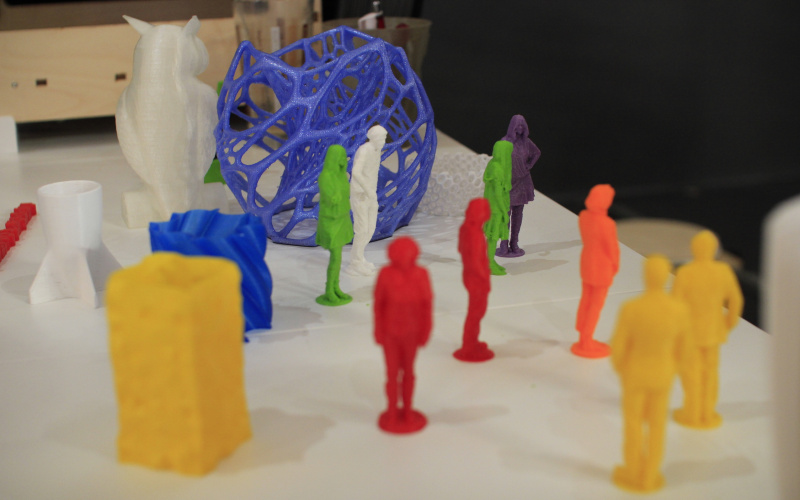 A lot of little colourful igurines printed with the 3D-printer are standing every which way on a table.
