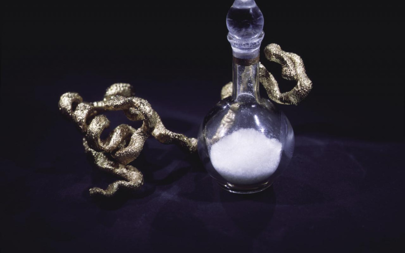 Sculpture of a glass vessel with white content and a golden cast in front of a black background