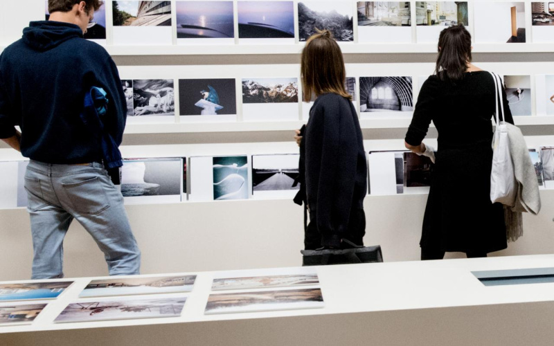 Drei Menschen betrachten Fotografien in einer Ausstellung