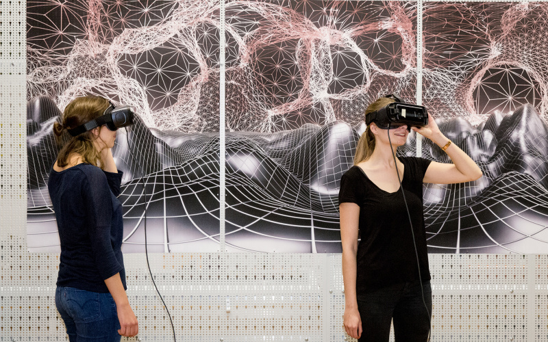 Zwei Frauen mit VR-Brillen stehen vor einer graphischen Landschaft