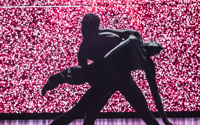 Die Silhouette zweier ineinander verwobener TänzerInnen vor einem pink angeleuchteten HIntergrund