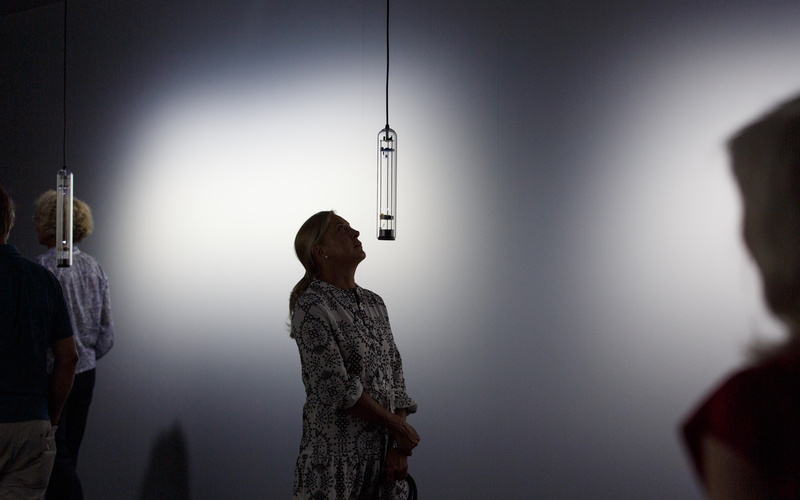 Das Bild zeigt eine Frau die auf eine Klanginstallation hochschaut die in längliches Glas gefasst ist