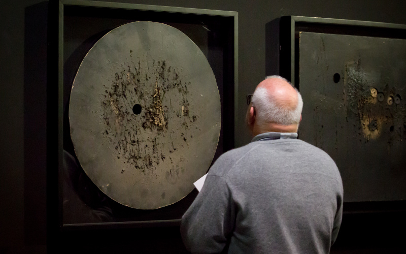  The photo shows the back of a bald man in front of a work by Aldo Tambellini.