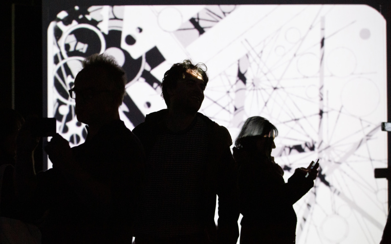 Photo of people in front of a projection screen with an abstract video in black and white - an impression of the exhibition »bauhaus.film.expanded« at the ZKM Karlsruhe.