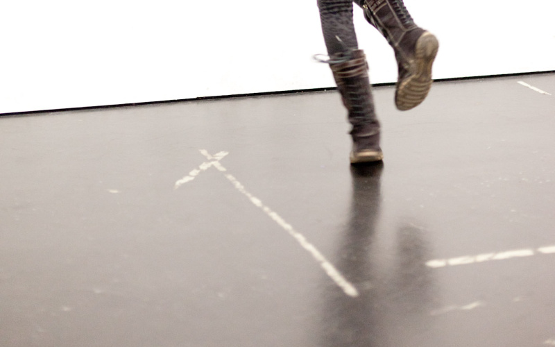 A girl is jumping with joy turning the back to the audience with both arms akimbo.