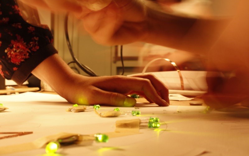 One can see a hand, that is leaning on a table on which - taped to a sheet of paper - green LEDs are glowing.