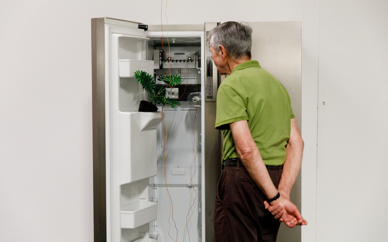 An elderly gentleman stands in front of an open refrigerator, which has been converted into a media installation. 