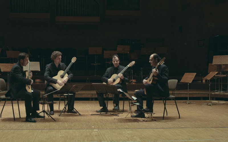 Four men are sitting in an open circle with guitars in their hands.