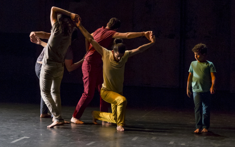 Four dancers dressed in colorful dancers in an intricate dance position and a green boy dressed in green.