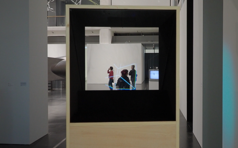 View through a box with a transparent plate into a room. An animated geometric figure can be seen in the room.