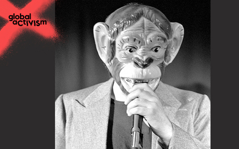 A man with a monkeymask speaks into a microphone