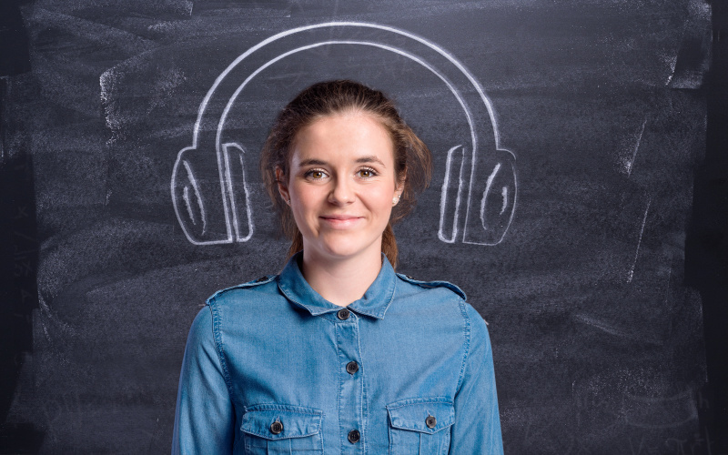 A woman is standing in front of a blackboard with headphones painted on.