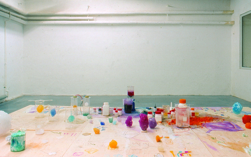 View of the exhibition "Fiction & Science». In the foreground a table with colorful crystals and chemicals.