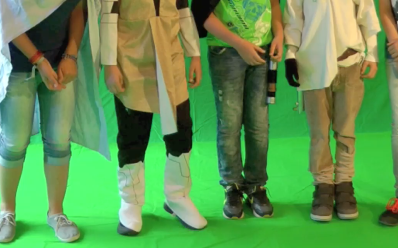 Fünf Kinder stehen nebeneinander vor einem Greenscreen - man kann nur ihre Beine sehen.