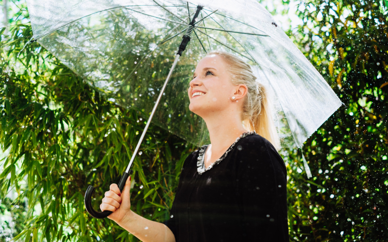Frau steht mit Regenschirm unter der Raindance-Installation
