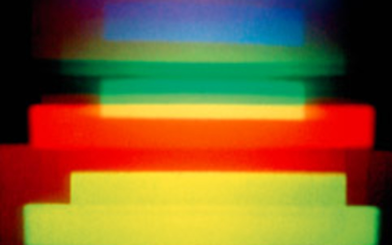 A holographic image by Dieter Jung. Red, blue, green and yellow horizontal stripes on a dark background.