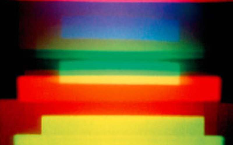 A holographic image by Dieter Jung. Red, blue, green and yellow horizontal stripes on a dark background.