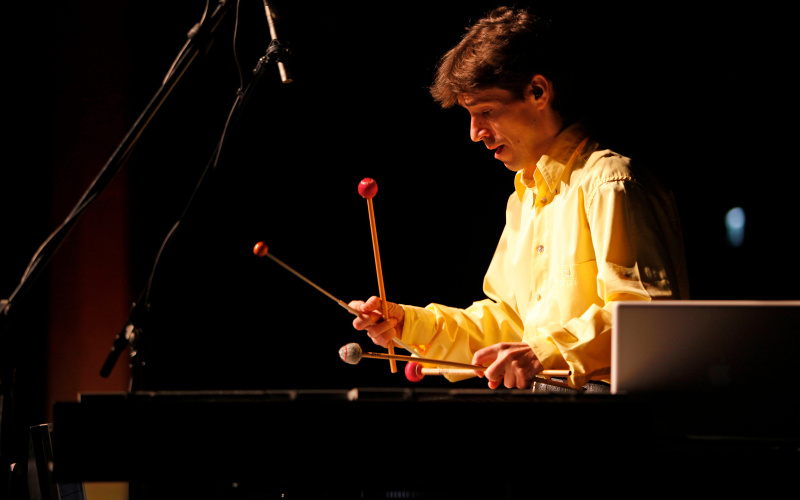 A man is playing on a big xylophone with four beaters holding two in each hand.