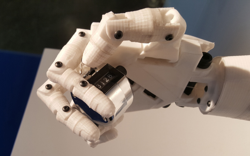 The photo shows a white robot hand holding a clicker.